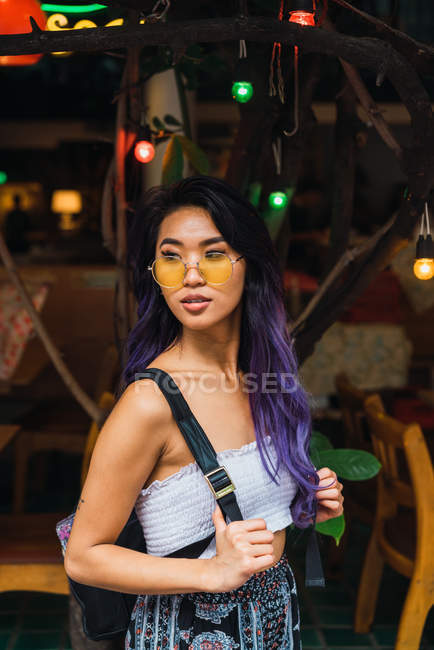 Жінка з фіолетовим волоссям позує на дереві з цибулинами — стокове фото