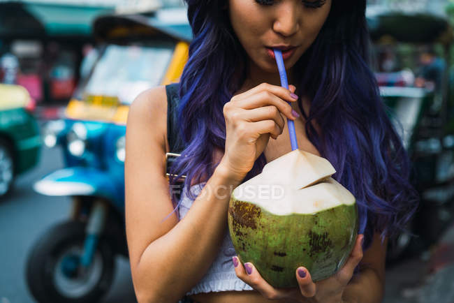 Кукурудза жінка з фіолетовим волоссям, що п'є з кокосового горіха з соломою на вулиці . — стокове фото