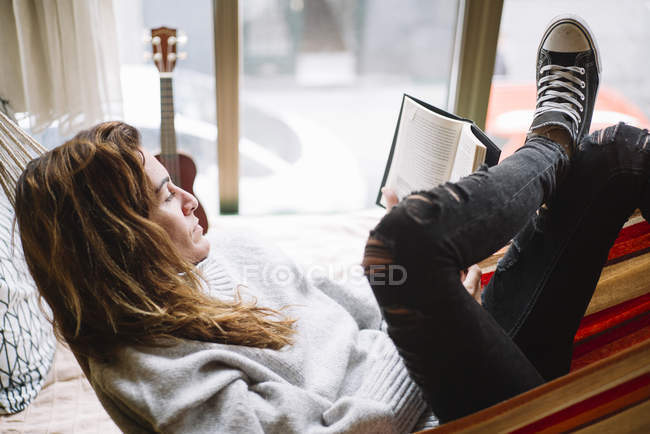 Mujer acostada en hamaca relajándose con libro - foto de stock