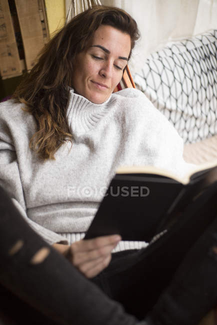 Morena mulher deitada em rede com livro — Fotografia de Stock