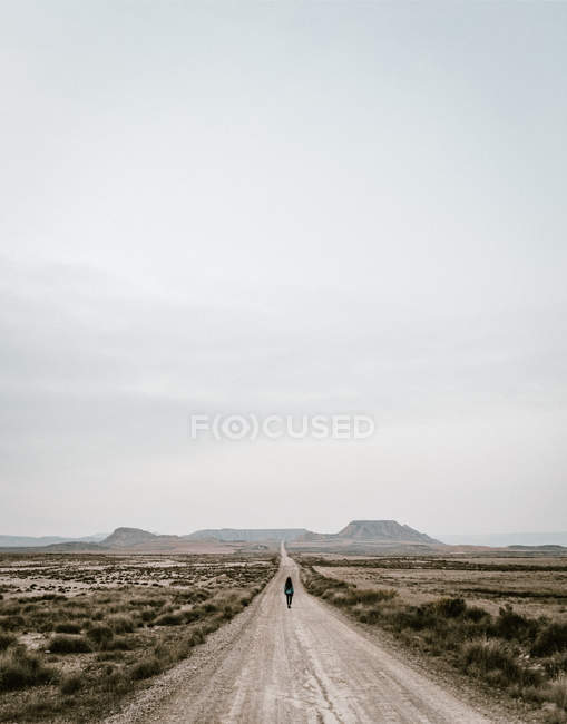 Persona irreconocible caminando por la carretera rural en el campo con hierba seca . - foto de stock