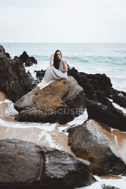 Brünettes Mädchen im Kleid sitzt auf Küstenfelsen — Stockfoto