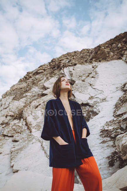 Topless brunette girl in black jacket standing at rocky cliff and looking up — Stock Photo