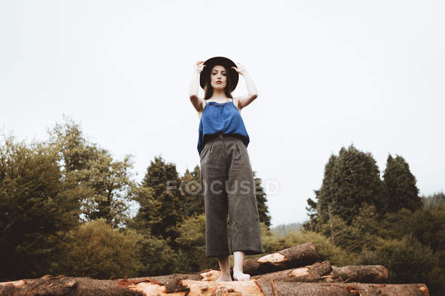 Sensual brunette woman posing with hat on log pile — Stock Photo