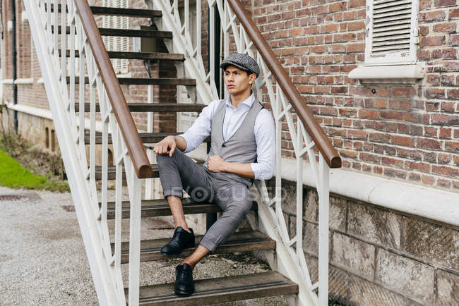 Cheerful man in vintage clothes and cap sitting on stairs — Stock Photo