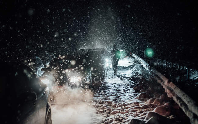 Pessoa irreconhecível de pé ao longo de carros presos na estrada na neve na noite de inverno . — Fotografia de Stock