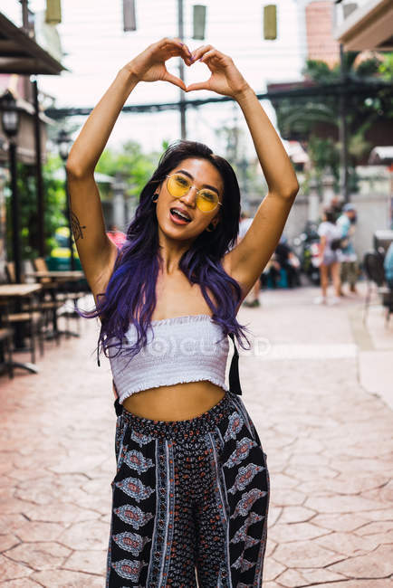 Mulher alegre com cabelo roxo gesticulando coração com as mãos na rua . — Fotografia de Stock