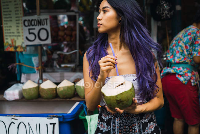 Молодая женщина с фиолетовыми волосами пьет из кокоса — стоковое фото