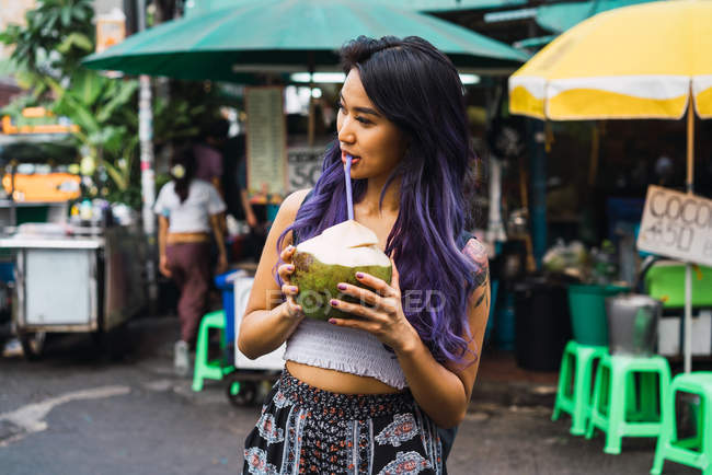 Молода жінка з фіолетовим волоссям п'є з кокосового горіха на вулиці — стокове фото