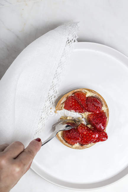 Crop hand taking piece of tart with red strawberries — Stock Photo