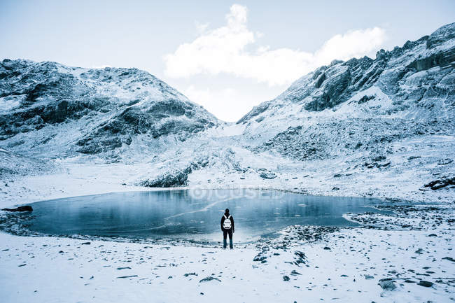 Vista trasera del turista parado en el lago helado en las montañas nevadas
. — Stock Photo