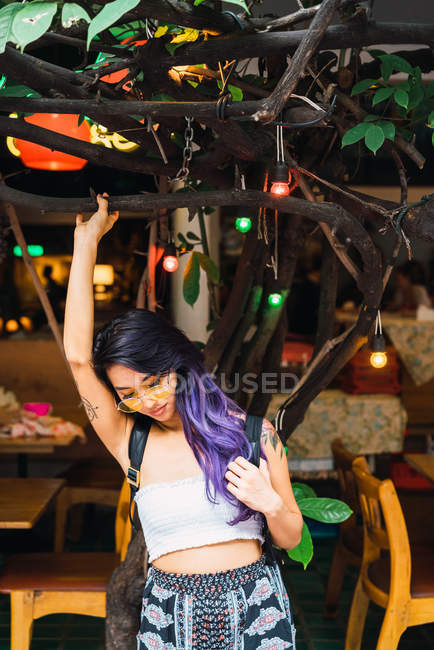 Hübsche Frau mit lila Haaren posiert an Baum mit Glühbirnen auf Stadtstraße. — Stockfoto