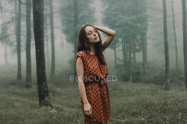 Jeune brunette en robe debout dans des bois effrayants — Photo de stock