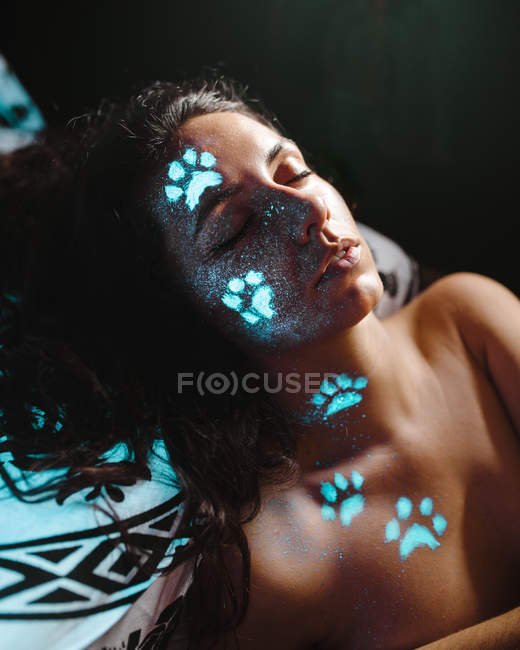 Jeune femme avec des empreintes de pattes d'animaux fluorescentes bleues sur le visage avec les yeux fermés . — Photo de stock