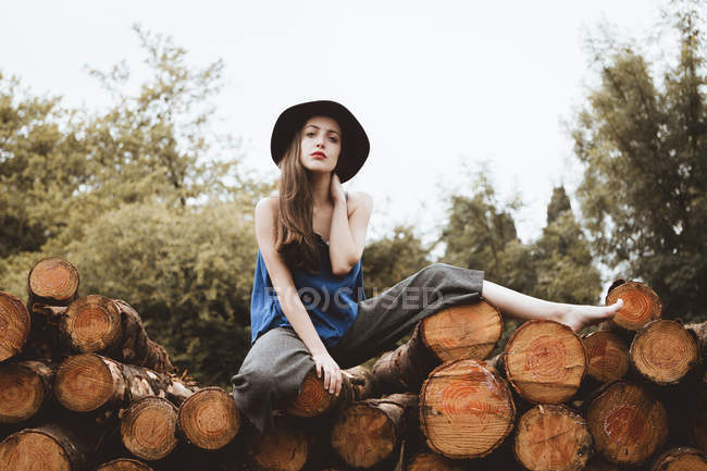 Elegante donna in cappello in posa su log pile — Foto stock