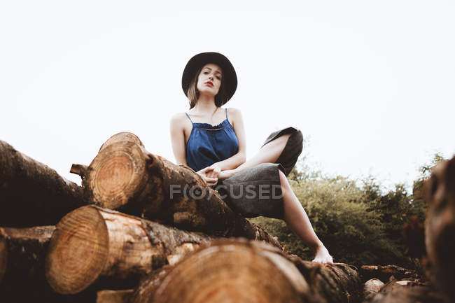 Stylish brunette woman in hat posing on log pile — Stock Photo