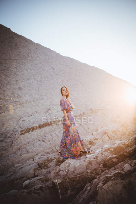 Вид сбоку на юную брюнетку в длинном платье, позирующую на скале — стоковое фото