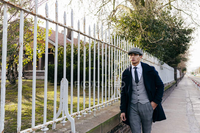 Man in vintage clothes walking near gate at street scene — Stock Photo