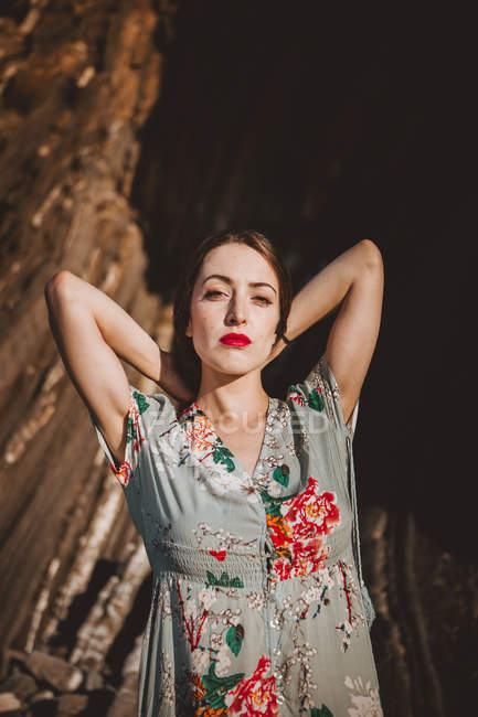 Young brunette with red lips wearing elegant ornamental dress posing in sunlight. — Stock Photo