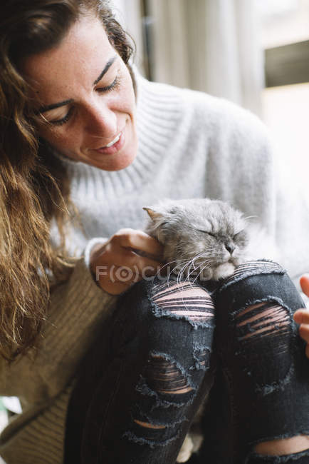 Усміхнена жінка погладжує кота на коліна — стокове фото