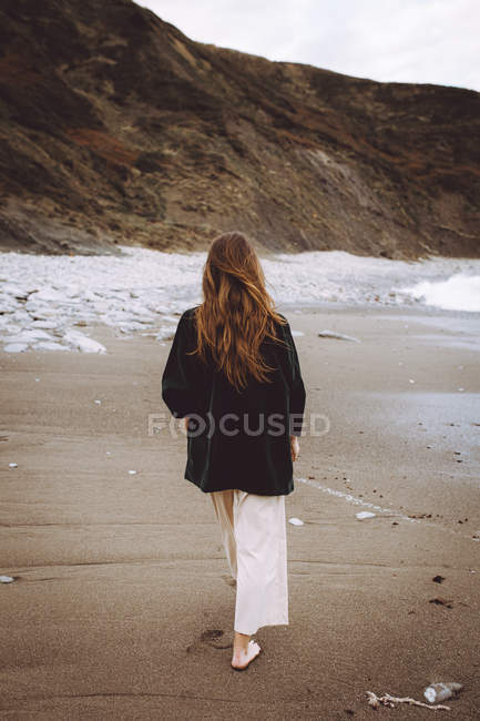 Вид ззаду жінки, що йде уздовж берегової лінії океану — стокове фото