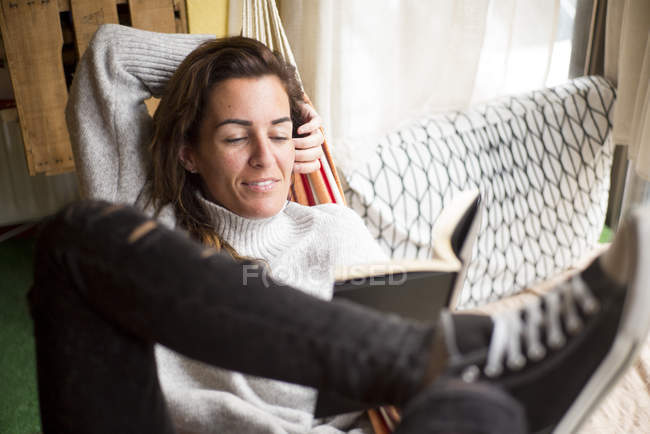 Mulher em rede relaxante com livro — Fotografia de Stock
