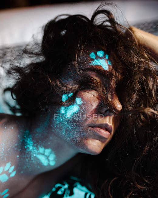 Femme avec des empreintes fluorescentes de pattes de chat sur le visage — Photo de stock