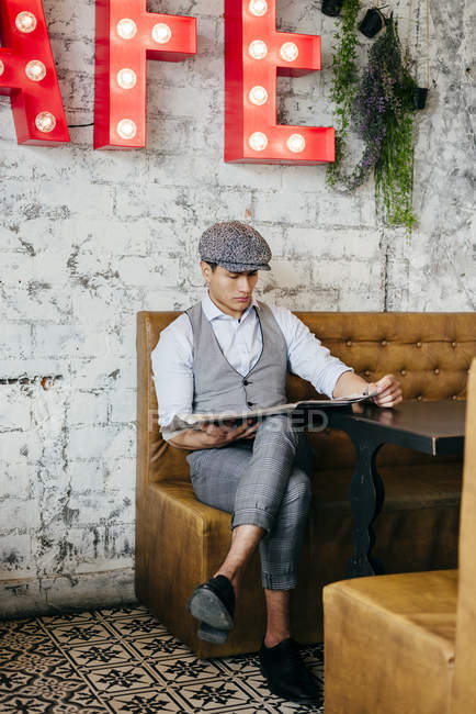 Hombre con ropa vintage sentado en la mesa del café y leyendo el periódico - foto de stock