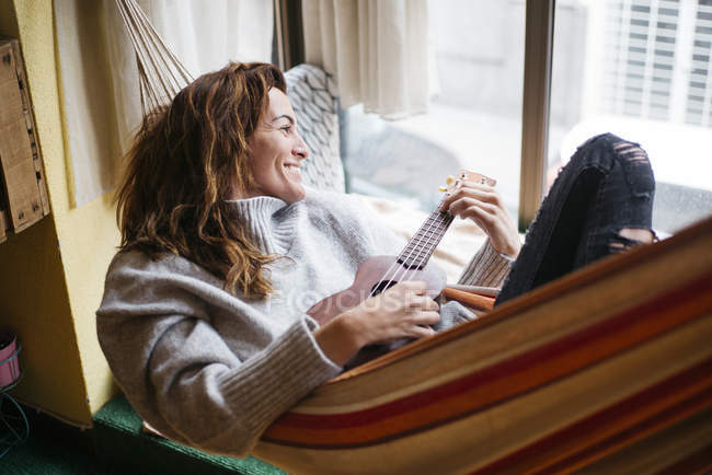 Morena mulher em rede jogando ukulele — Fotografia de Stock