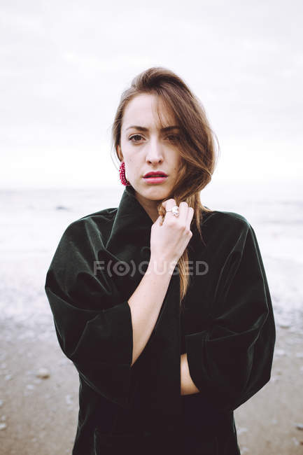 Молода жінка в чорній куртці позує на березі океану — стокове фото