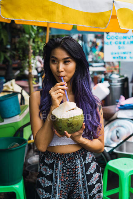 Азиатка пьет с соломой из кокоса — стоковое фото