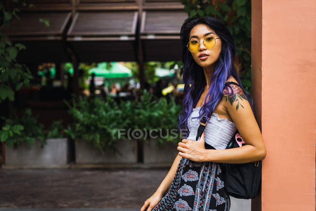 Giovane donna con i capelli viola posa in occhiali da sole gialli in strada e guardando la fotocamera — Foto stock