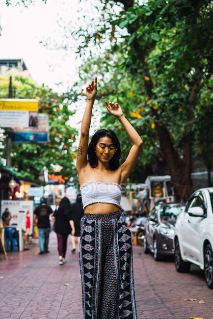 Hübsche junge Frau posiert mit erhobenen Armen auf der Straße — Stockfoto