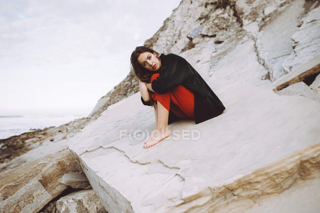 Stylish brunette sitting on shore rocks — Stock Photo