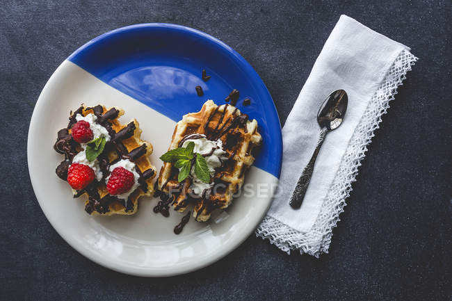 Directly above homemade waffle with cream raspberries and chocolate strawberries served with spoon on napkin — Stock Photo