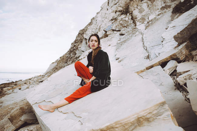 Stylisches brünettes Mädchen sitzt auf Uferfelsen — Stockfoto