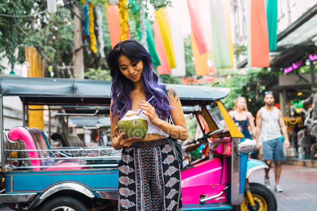 Mujer joven caminando con bebida de coco en la calle - foto de stock