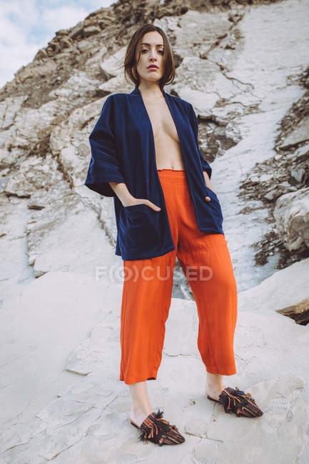 Junge selbstbewusste Frau in trendiger Jacke auf nacktem Körper posiert selbstbewusst vor der Kamera auf Stein. — Stockfoto
