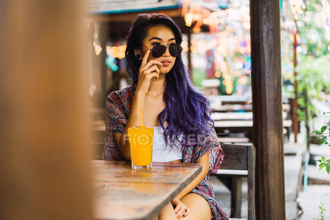 Молодая женщина позирует в солнечных очках за столиком в кафе — стоковое фото