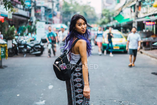 Femme aux cheveux violets posant sur la rue et regardant par-dessus l'épaule à la caméra — Photo de stock
