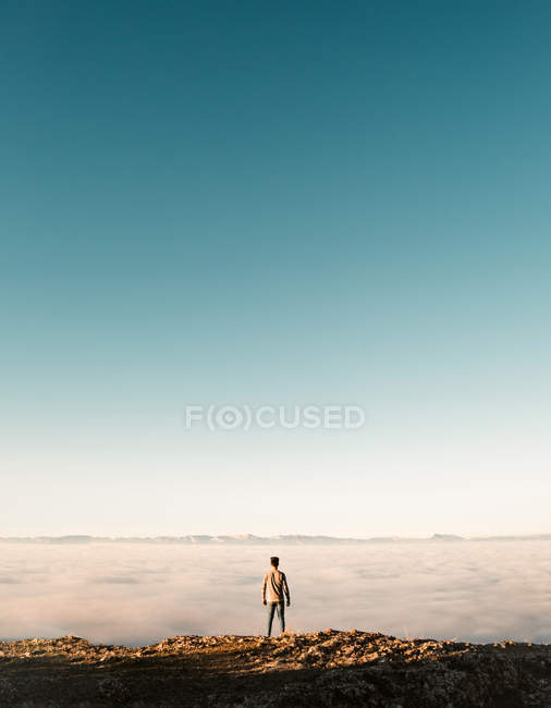 Rückansicht eines Touristen, der an einer Felskante über der Wolkenlandschaft steht. — Stockfoto