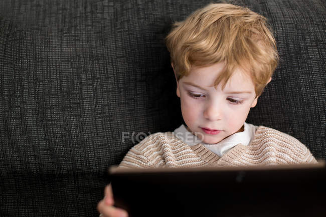 Blonde garçon couché sur le canapé avec tablette — Photo de stock