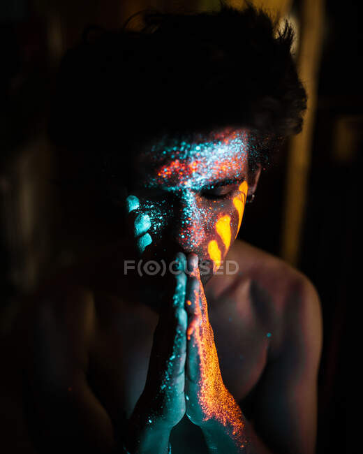 Young man with stacked hands with different fluorescent paint on face. — Stock Photo