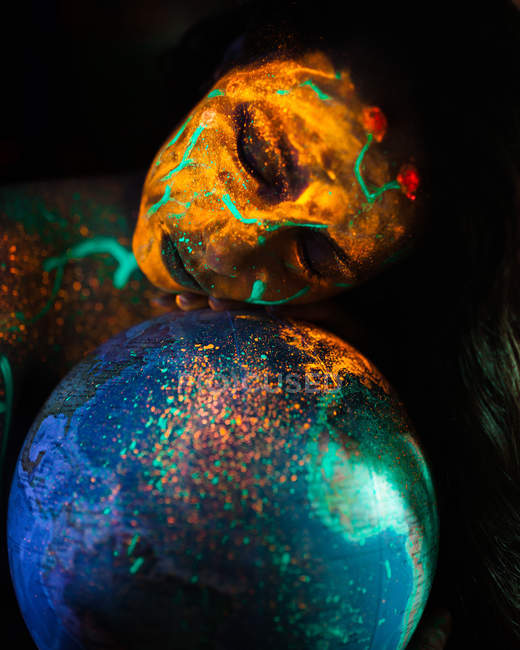 Junge Frau mit fluoreszierender Farbe und Globus-Modell überzogen. — Stockfoto