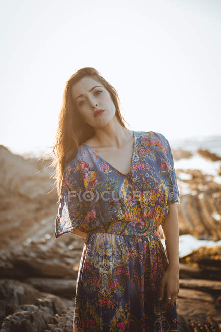 Брюнетка в платье с цветочным узором, позирующая на скалистой местности — стоковое фото