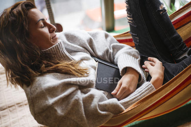 Mujer durmiendo en hamaca con libro - foto de stock