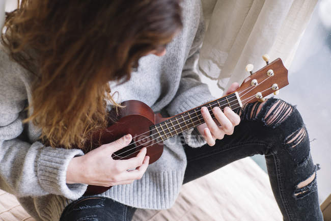 Crop femme brune jouant ukulele à la maison — Photo de stock