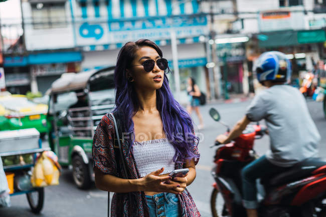 Mujer joven en gafas de sol con smartphone en las manos en la calle de la ciudad . - foto de stock