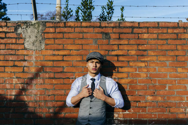 Man in cap standing at brick wall and looking at camera — Stock Photo