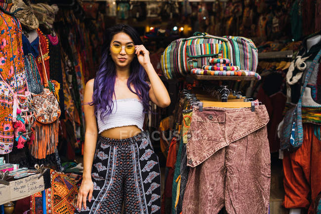Young Asian woman in sunglasses standing in clothes shop. — Stock Photo